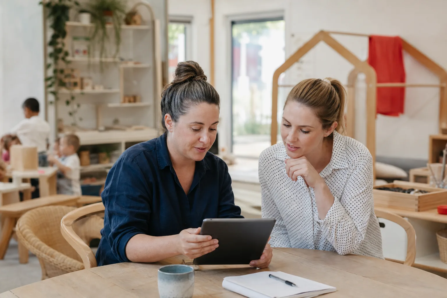 Early-learning centre director and educator reviewing staff onboarding on a tablet in a childcare classroom